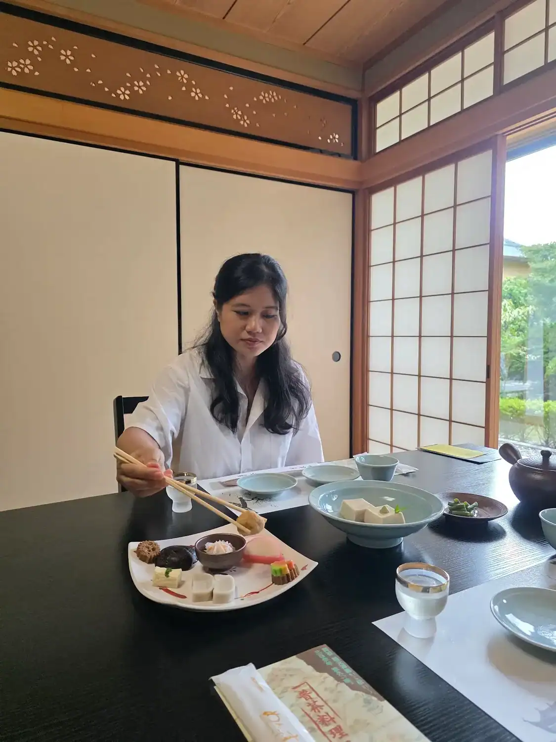 woman enjoying a kaiseki meal inside a traditional Japanese dining room with shoji doors and a neatly arranged set of dishes in our 2 day Kyoto Itinerary