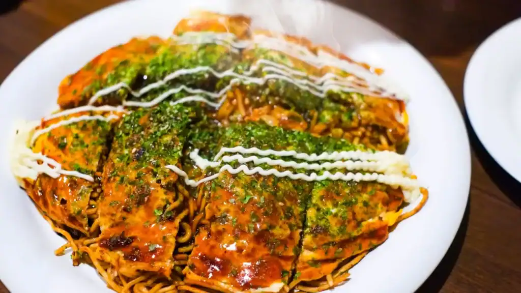 Hiroshima-style okonomiyaki layered with noodles, egg, and savory sauce—one of the regional Japanese foods travelers must try.