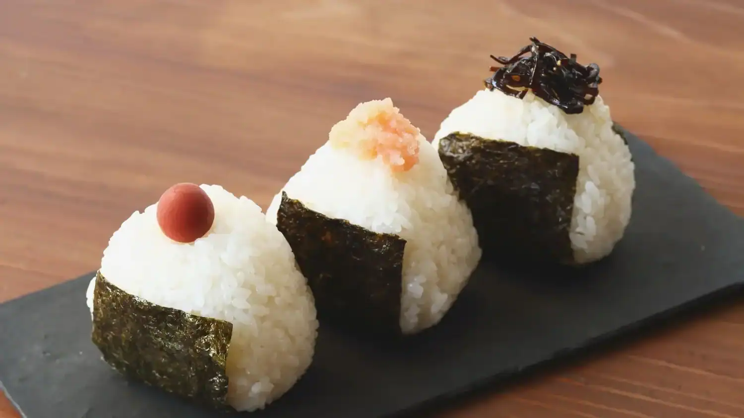 Three Japanese onigiri rice balls wrapped in nori, each topped with different fillings like ume, mentaiko, and kombu—one of the top Japanese foods to try in Japan.