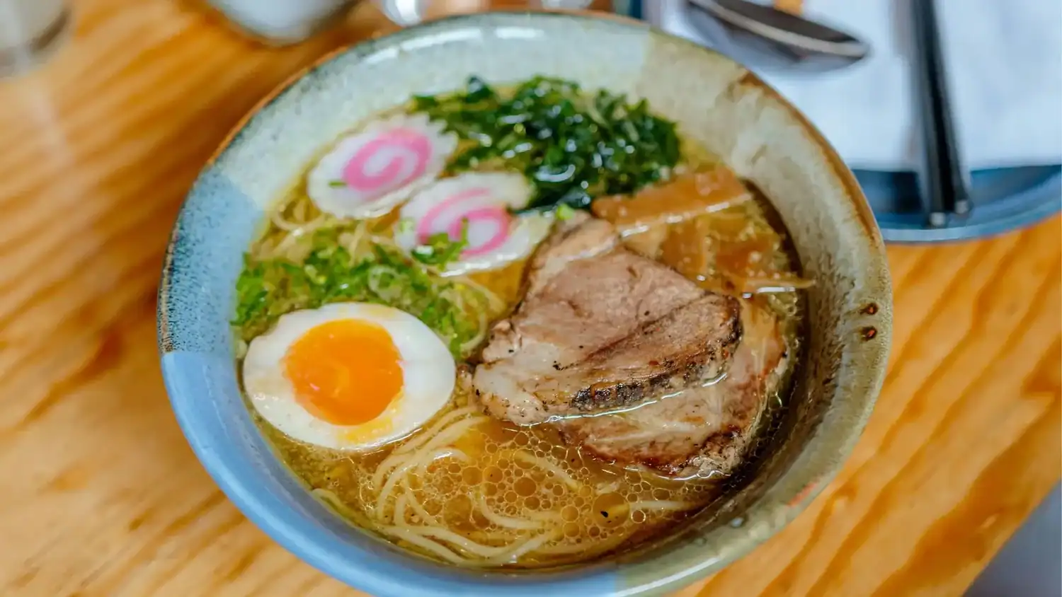 Bowl of Japanese ramen with soft-boiled egg, chashu pork, noodles, and narutomaki in rich broth.