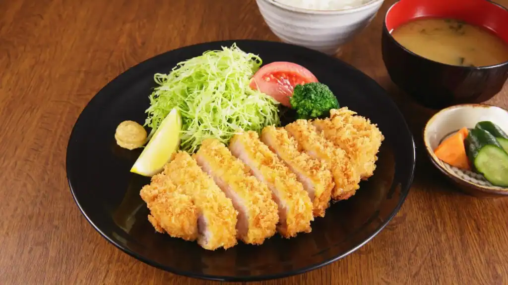 Japanese tonkatsu pork cutlet served with shredded cabbage, lemon, rice, and miso soup.