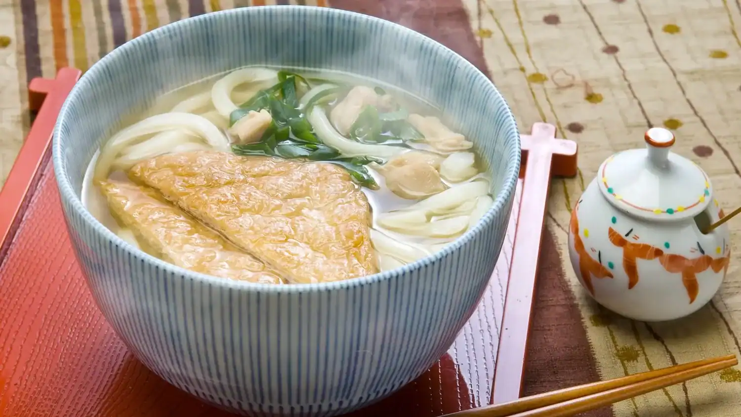 Steaming bowl of Japanese udon noodles in broth with aburaage tofu and green onions.