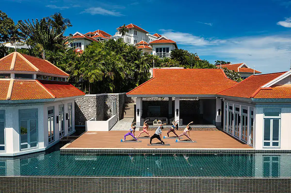A group go through various yoga positions on the sunlit deck of Amatara Resort, one of best luxury wellness retreats in Phuket.