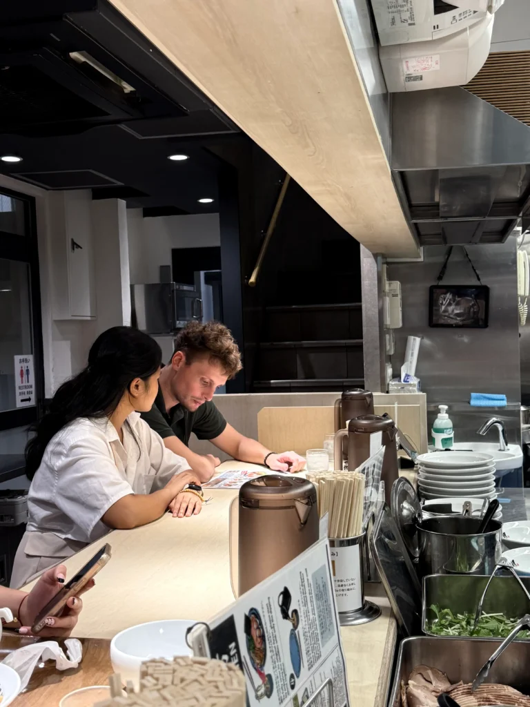 Things to Do in Osaka -  cozy ramen bar with open kitchen counter where diners watch chefs prepare dishes.