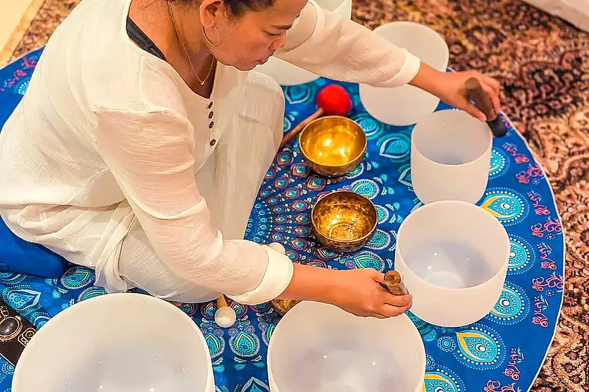 A woman in traditional white robes sits cross-legged on a blue rug with bowls and oils, offering a glimpse into the cultural sessions of Hilltop Wellness Resort, one of the best wellness retreats in Phuket.