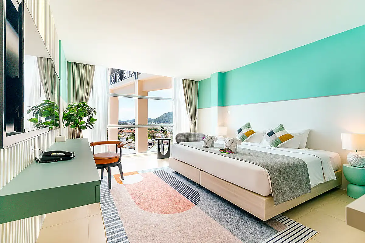 A bedroom with seafoam green accents in Hilltop Wellness Resort. The room is bright, with a clear view of the nature in the area.