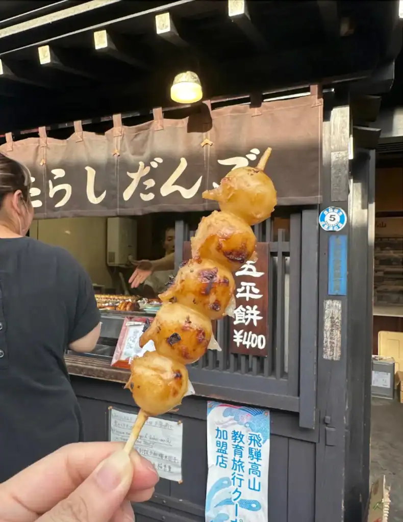Best street food in Tokyo shown through grilled dango skewers held in front of a traditional street food stall