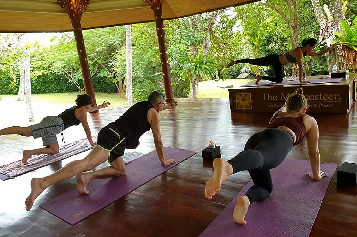 People slowly raise their legs while following the instructor's demonstration in Mangosteen, which offers one of the top wellness retreats in Phuket.