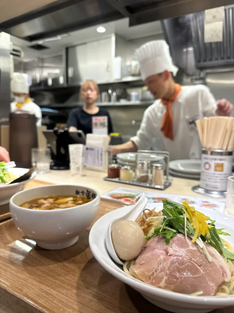 Ramen served at a counter-style Japanese restaurant with a chef preparing dishes, showcasing restaurant etiquette in Japan at counter seating. Restaurant Etiquette in Japan