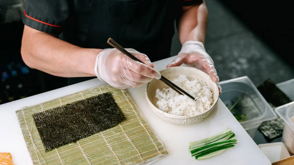 Things to Do in Osaka joining a sushi making class with hands preparing rice nori and fresh ingredients at a cooking station.