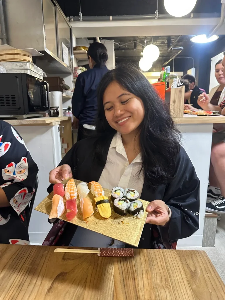 A traveler holding a plate of handmade sushi during a sushi-making class in Japan, learning restaurant etiquette in Japan.