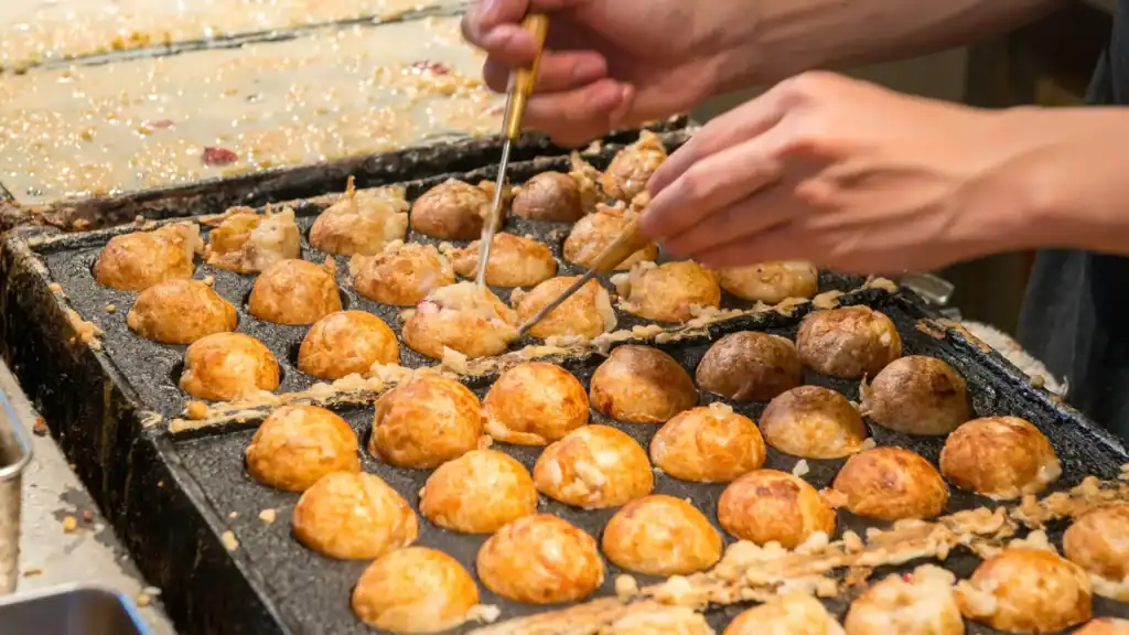 Best street food in Tokyo shown through takoyaki being cooked on a hot grill at a busy street food stall