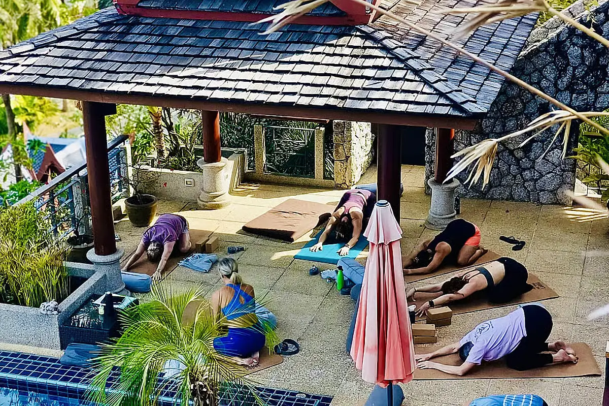Several yogi are working on their flexibility on the large deck of a traditional Thai building.