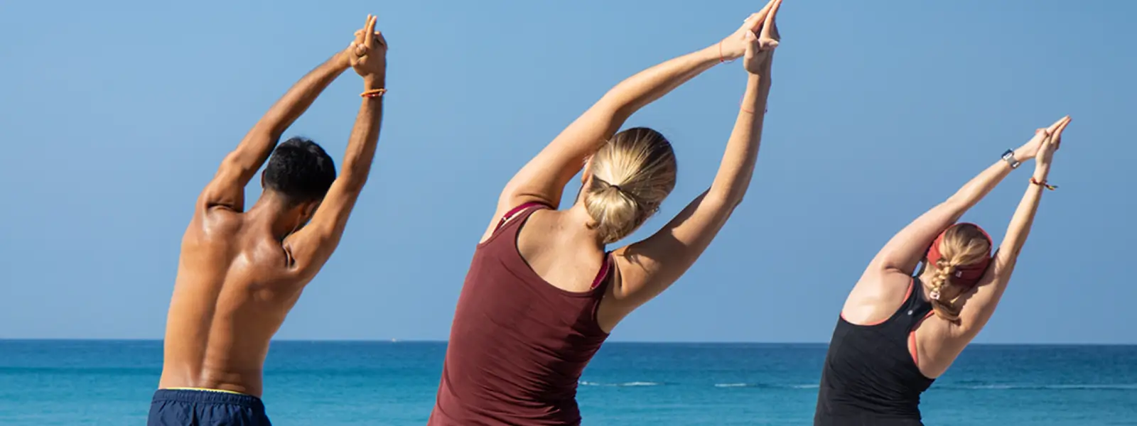 Three people have their arms raised as they stretch to their right side, taking part in the yoga teacher training program in Phuket.