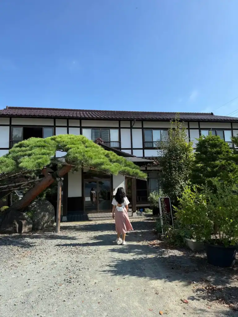 Entrance of Komaya Ryokan in Kawaguchiko on a clear day, traditional Japanese ryokan surrounded by greenery and a quiet garden path.