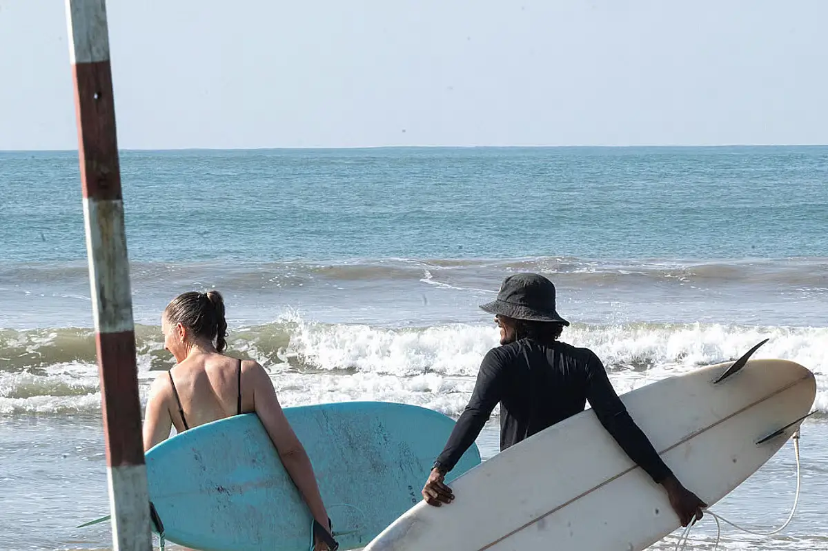 Two people holding surfboards while looking slightly to the side and toward the ocean.