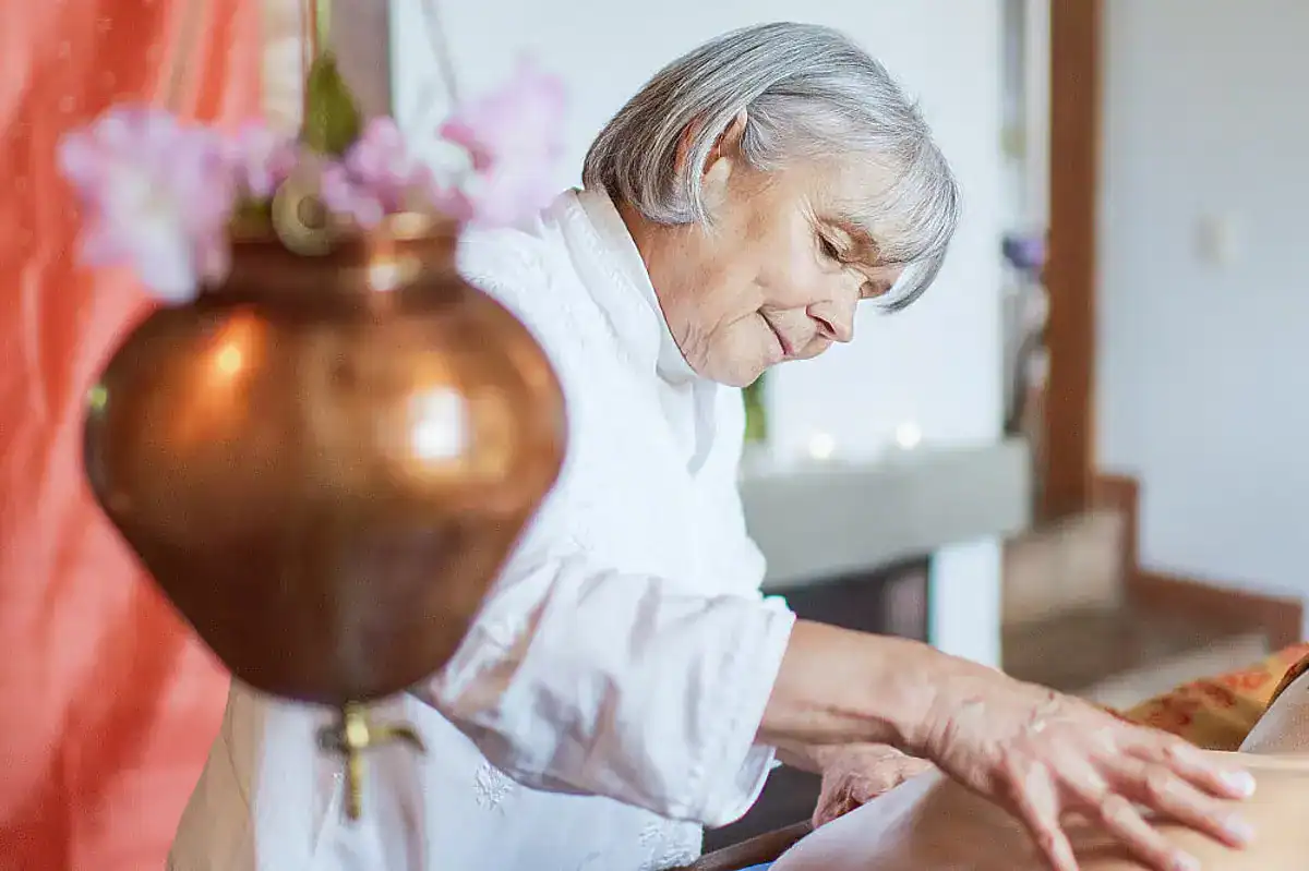 An elderly staff member massages the back of a person.