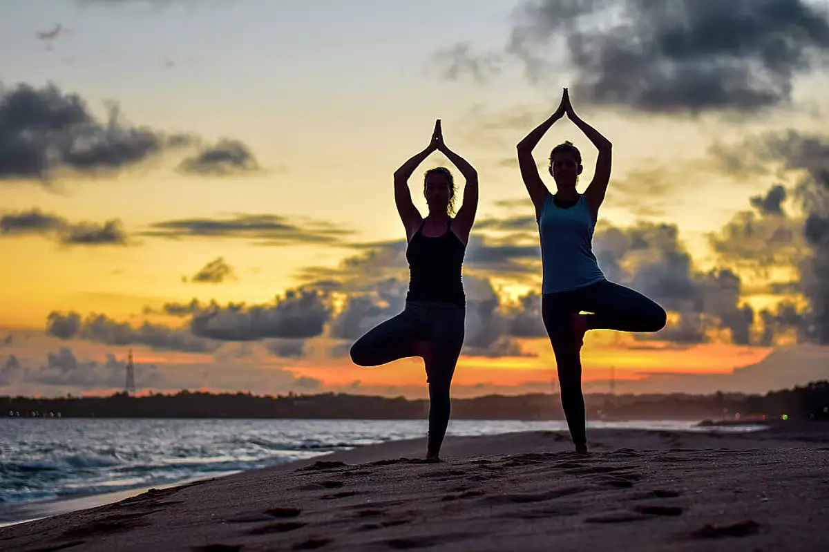 Two people holding a yoga pose against a sunset.