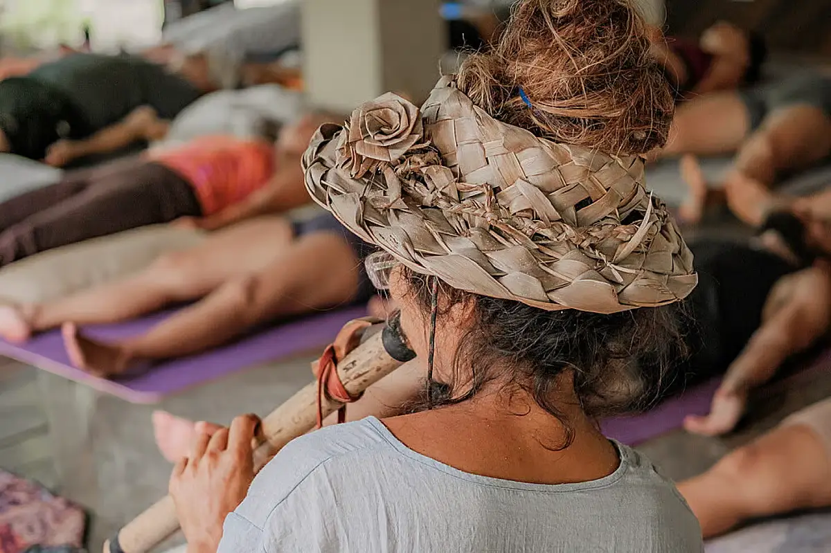Yogis lay on mats while an elderly woman plays a tune on a traditional wind instrument.