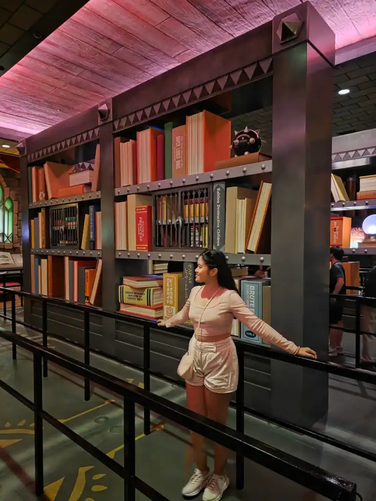 Woman wearing white sneakers standing in front of a large decorative bookshelf display indoors.