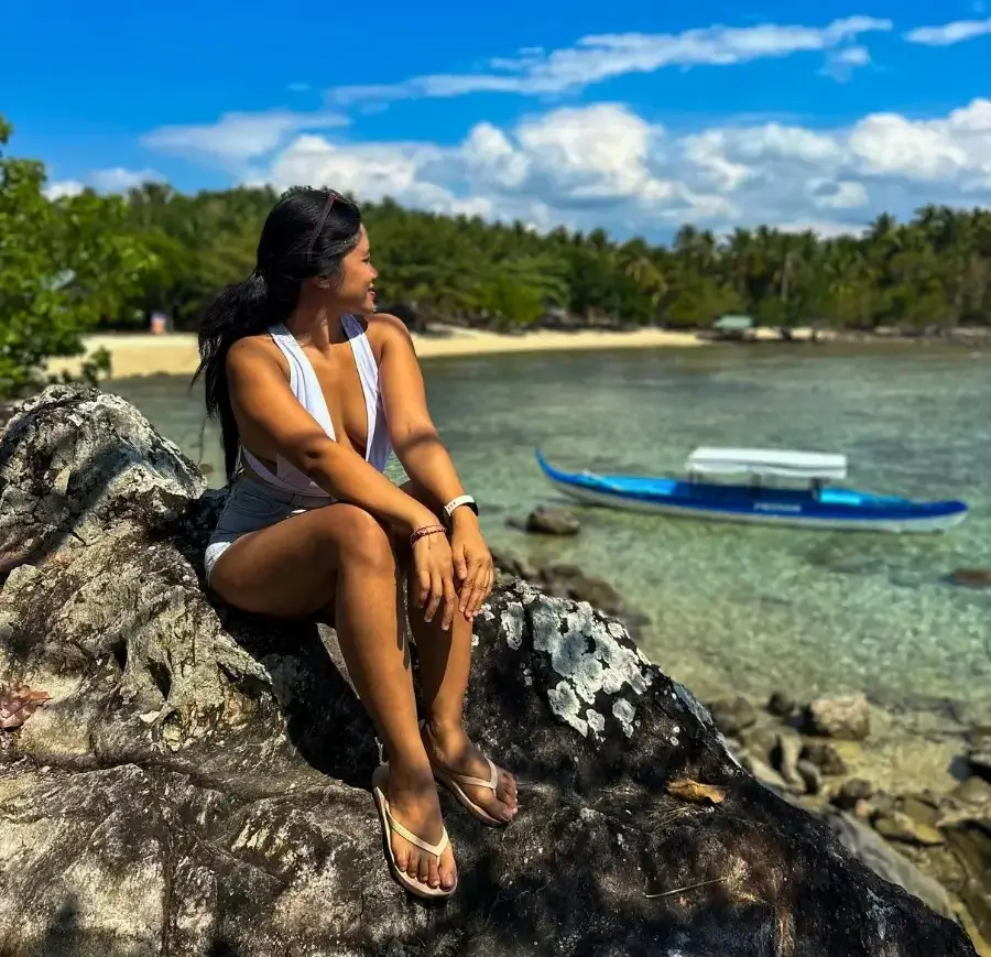 A woman sits by the rocks near a beach.