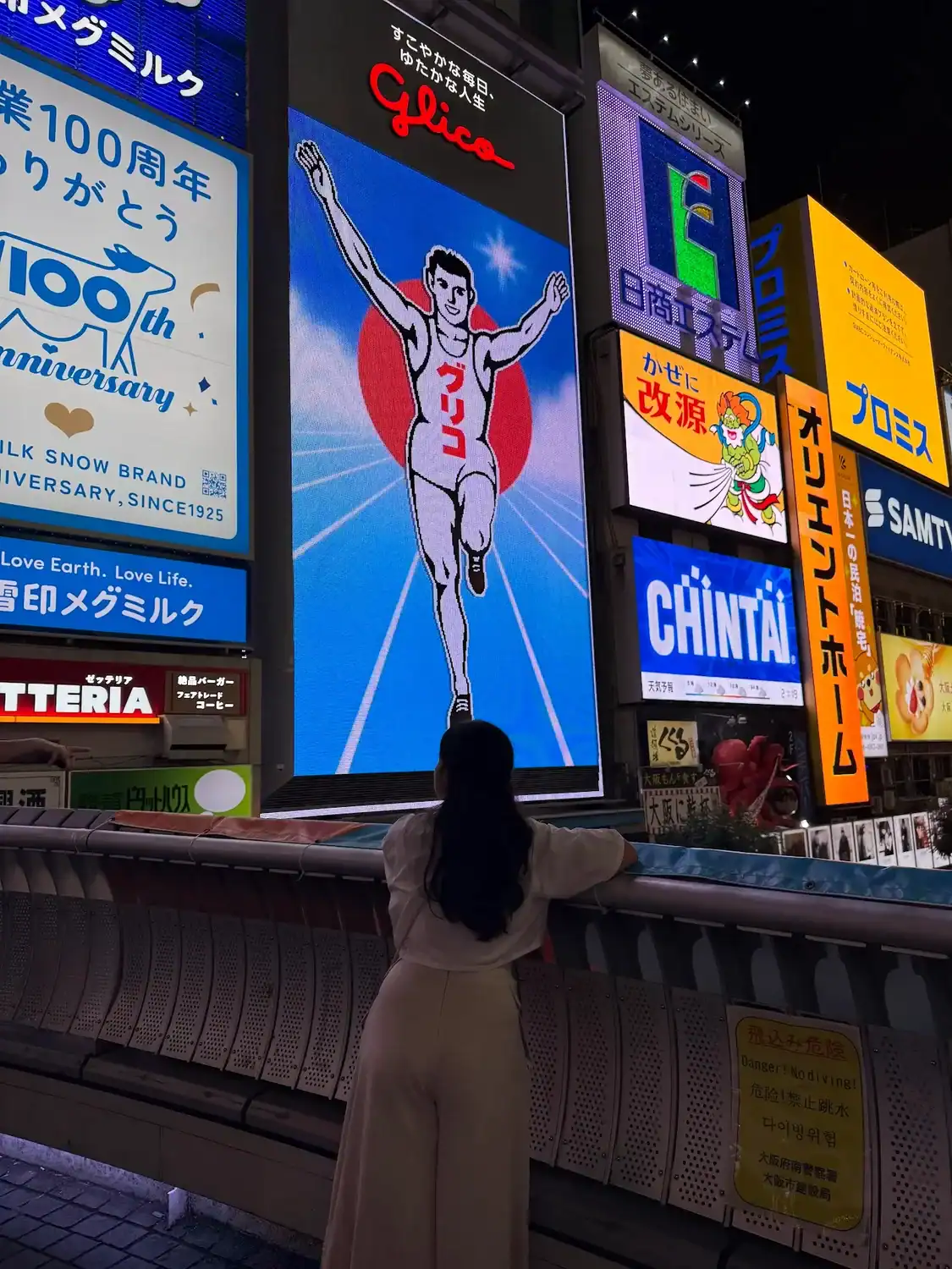 Traveler overlooking the Glico Running Man sign in Dotonbori at night, one of the most iconic areas featured in this guide on where to stay in Osaka.