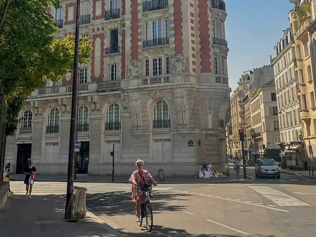 Historic Parisian apartment building on a quiet neighborhood street with a cyclist passing by. Something you will encounter as someone who volunteer in Paris. 