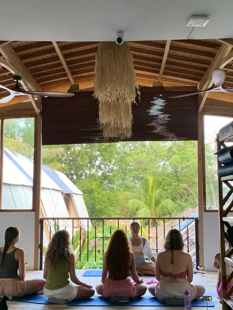 Yoga instructor leading a small class in an open-air studio surrounded by tropical greenery at a wellness hostel where certified teachers can volunteer in Bali.