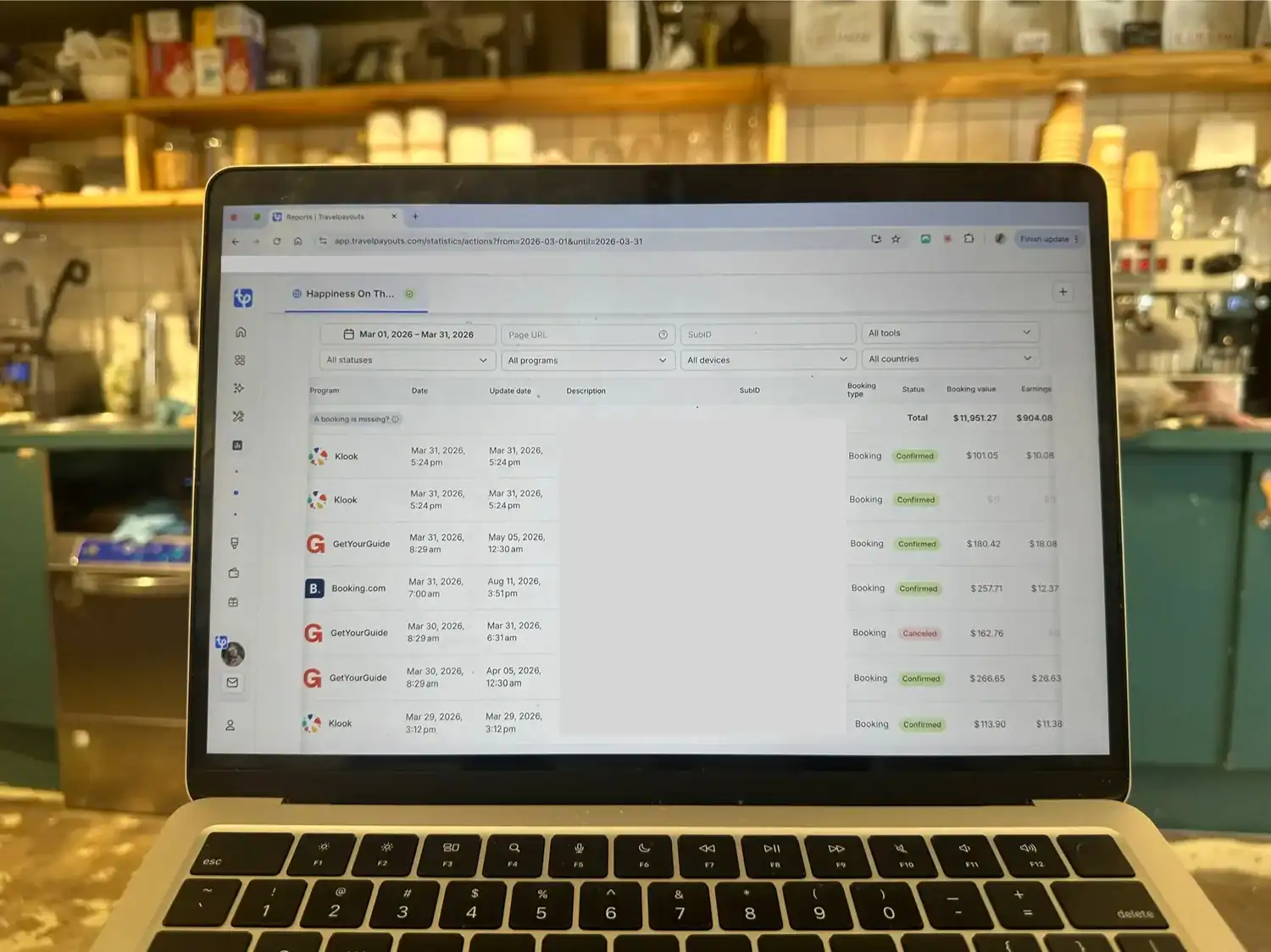 Laptop screen showing the Travelpayouts bookings dashboard for March 2026, open at a café table