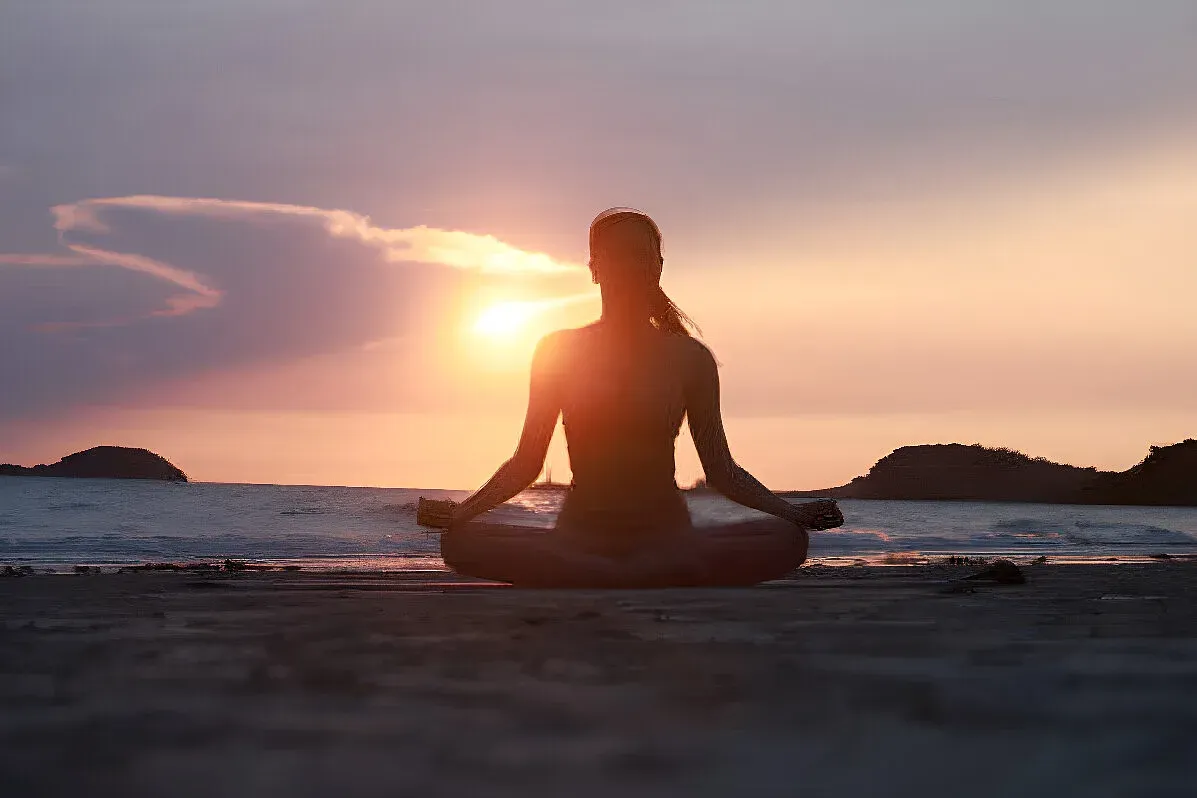 Silhouette of a person meditating cross-legged on a beach at sunset