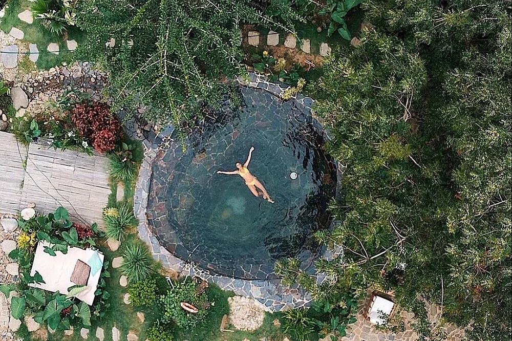 Aerial view of a woman floating in a round stone plunge pool surrounded by tropical plants at a self-love retreat in Colombia