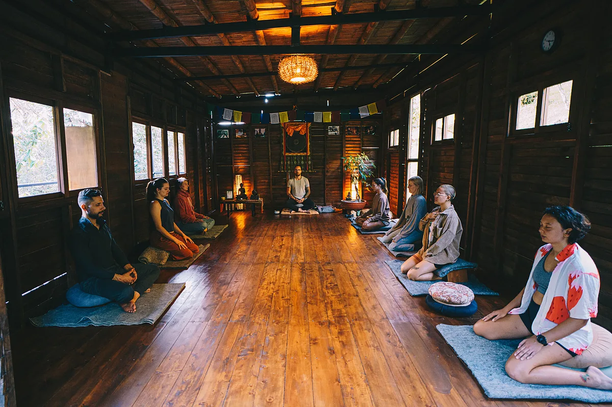 Group meditating on cushions in a wooden temple-style hall at a meditation and yoga retreat in Guatapé, Colombia