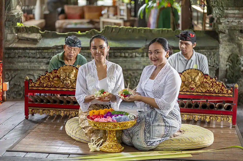 Two women in Balinese ceremonial dress holding flower offerings at a healing retreat in Sayan, Bali