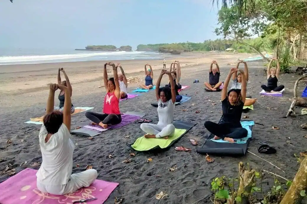 Group yoga session on a black sand beach at a wellness retreat in Bali